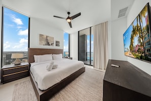 Una habitación de hotel moderna con una cama grande, un ventilador de techo, vistas a la ciudad, un ventanal amplio y un televisor de pantalla plana.