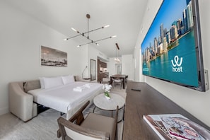A hotel room with a bed, a desk, a chair, a round table, a TV, and a cityscape view.
