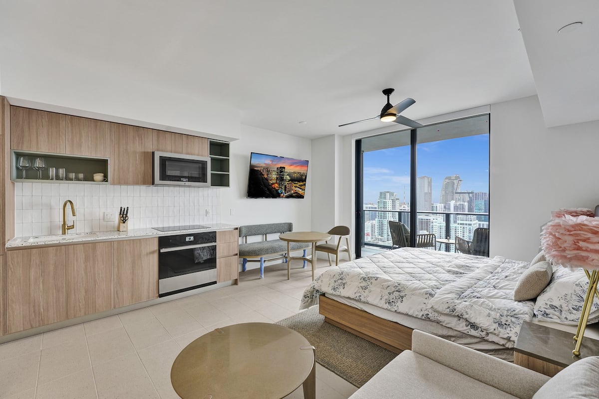 A modern apartment with a kitchen, dining area, and a large bed with a city view.