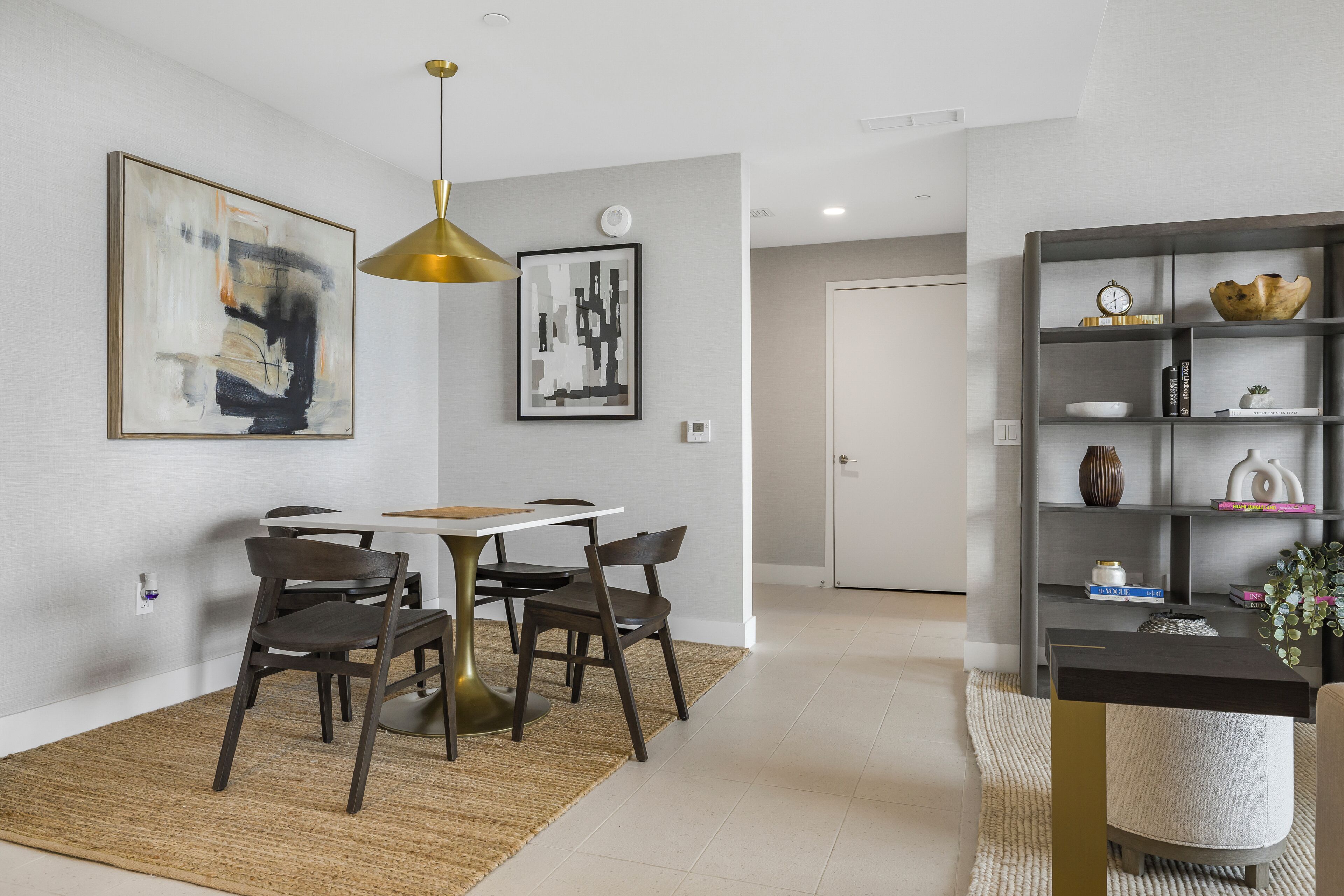 A modern dining area with a table and chairs, a hanging pendant light, and a bookshelf with decorative items.