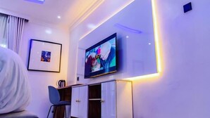 Moderni hotellihuone, jossa on seinälle asennettu taulutelevisio, työpöytä tuolilla ja seinällä kehystetty taulu.