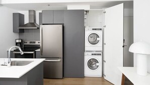 A compact kitchen with a built-in oven, a stainless steel refrigerator, and a washing machine.
