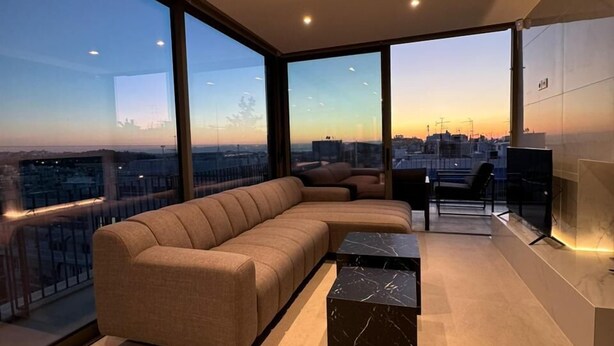 Una sala de estar moderna con un amplio sofá modular, una mesa de centro de mármol y vistas a la ciudad a través de grandes ventanales.