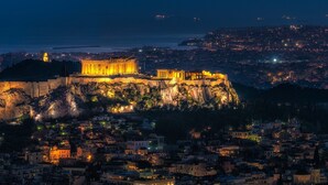 Un edificio histórico con arquitectura clásica, ubicado en una colina con vistas a una ciudad de noche.