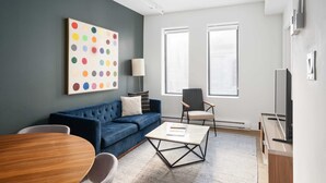 Un soggiorno moderno con un divano blu, un tavolino rotondo in legno e un'opera d'arte sulla parete con un motivo a pois colorati.