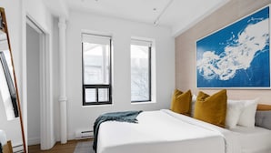 Camera da letto con un letto grande, due finestre, un quadro e pavimento in legno.