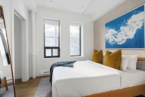 Une chambre avec un grand lit, deux fenêtres, un tableau au mur et un plancher en bois.