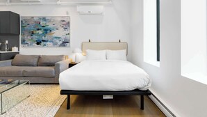 Un hotel moderno con una cama, un sofá, una mesita de vidrio y un cuadro abstracto grande en la pared.