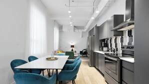 A modern kitchen with stainless steel appliances, a dining area with teal chairs, and a visible window. - Modern One-Bedroom|Downtown Steps from Centre Bell (Montréal)