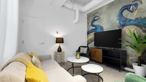 A modern living room with a sofa, a TV, a painting, and a plant. - Modern One-Bedroom|Downtown Steps from Centre Bell (Montréal)
