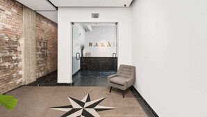 A modern interior with a brick wall, a glass door with 'BAKAI' signage, a marble floor, and a star-patterned rug. - Modern One-Bedroom|Downtown Steps from Centre Bell (Montréal)
