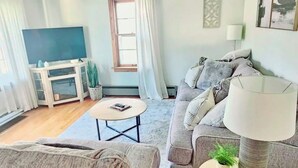 A living room with a sofa, a coffee table, a lamp, and a television. - Stumble-In Guest House- Downtown Location (Hermann)