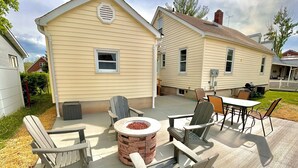 A patio area with Adirondack chairs, a round table, and a brick fire pit. - Stumble-In Guest House- Downtown Location (Hermann)
