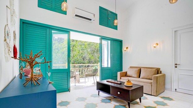 Una habitación con contraventanas color turquesa, un sofá, una mesa de centro y un suelo estampado.