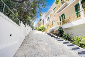 A narrow cobblestone pathway leading to a building with white walls and green shutters.