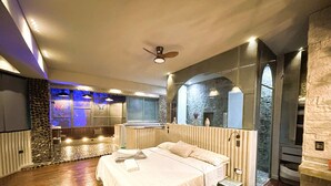 A spacious bedroom with a large bed, a sitting area with a view, and a stone wall. - EleMYNT LifeStyle Hotel (Guatapé)