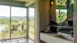 A balcony with a view of a lake and hills, a stone wall, and a fireplace. - EleMYNT LifeStyle Hotel (Guatapé)
