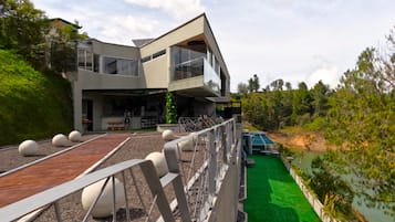 Una casa moderna de dos pisos con balcón, césped verde y vista al río.