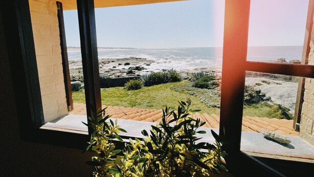Vue depuis une chambre dotée de grandes fenêtres donnant sur une plage rocheuse et l’océan.