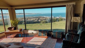 Un salon spacieux doté d’une grande fenêtre offrant une vue sur l’océan et le paysage rocheux.