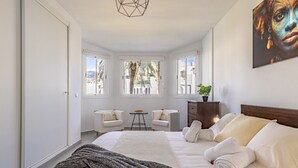 A bedroom with a bed, two chairs, a small table, and a cabinet. - Casa Chic de Ensueño, BBQ Azotea, 9 Piscinas, Golf (Marbella)