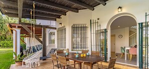 Relax in a serene outdoor space with a round table, wicker chairs, and a rope swing under a covered pergola.