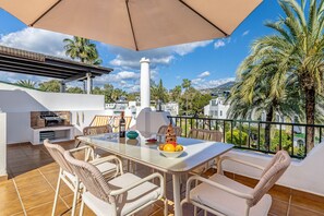 A terrace with a table, chairs, a grill, and a view of the city.