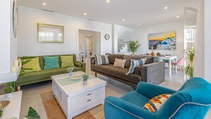 A modern living room with a green sofa, a brown sofa, a blue armchair, and a white coffee table. There is a painting on the wall and a staircase leading to another level. - Casa Chic de Ensueño, BBQ Azotea, 9 Piscinas, Golf (Marbella)