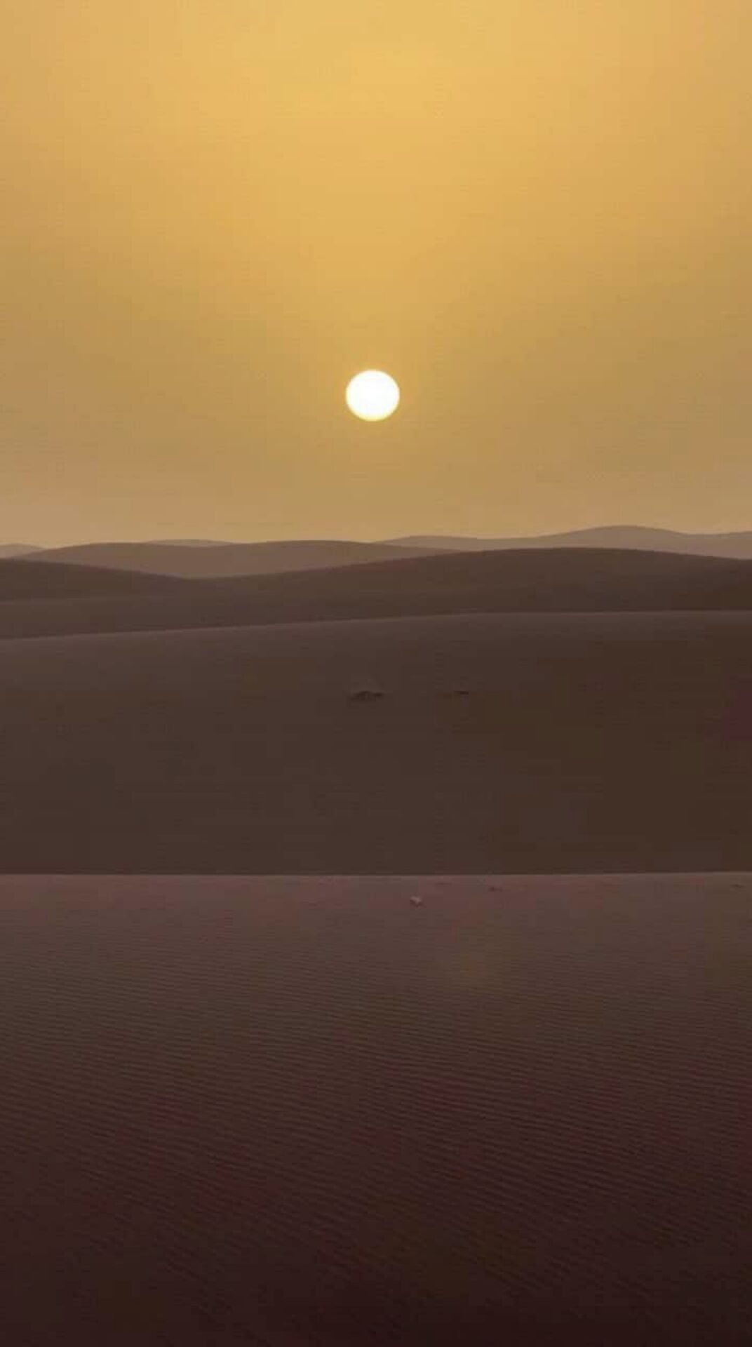A desert landscape with a large sun in the sky and distant hills.