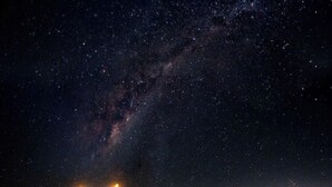 A desert landscape at night with a starry sky and a person standing in the distance.