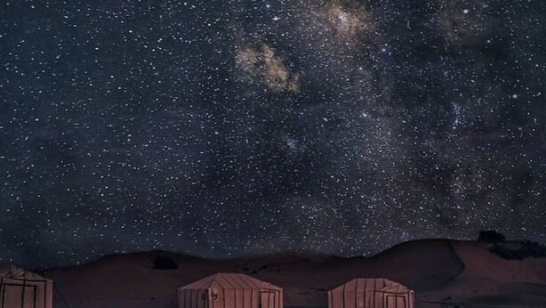 A person sitting by a campfire in a desert at night with a starry sky.
