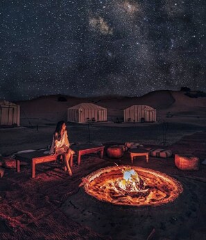 A person sitting by a campfire in a desert at night with a starry sky. - Merzouga Camel Ride & Overnight Desert Camp (Merzouga)