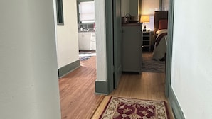 Ein Flur mit einem gemusterten Teppich, der zu einem Schlafzimmer mit einem Bett und einem Nachttisch führt.
