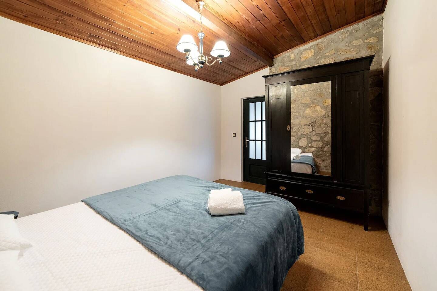 Une chambre avec un lit, une armoire, un mur en pierre et un plafond en bois.