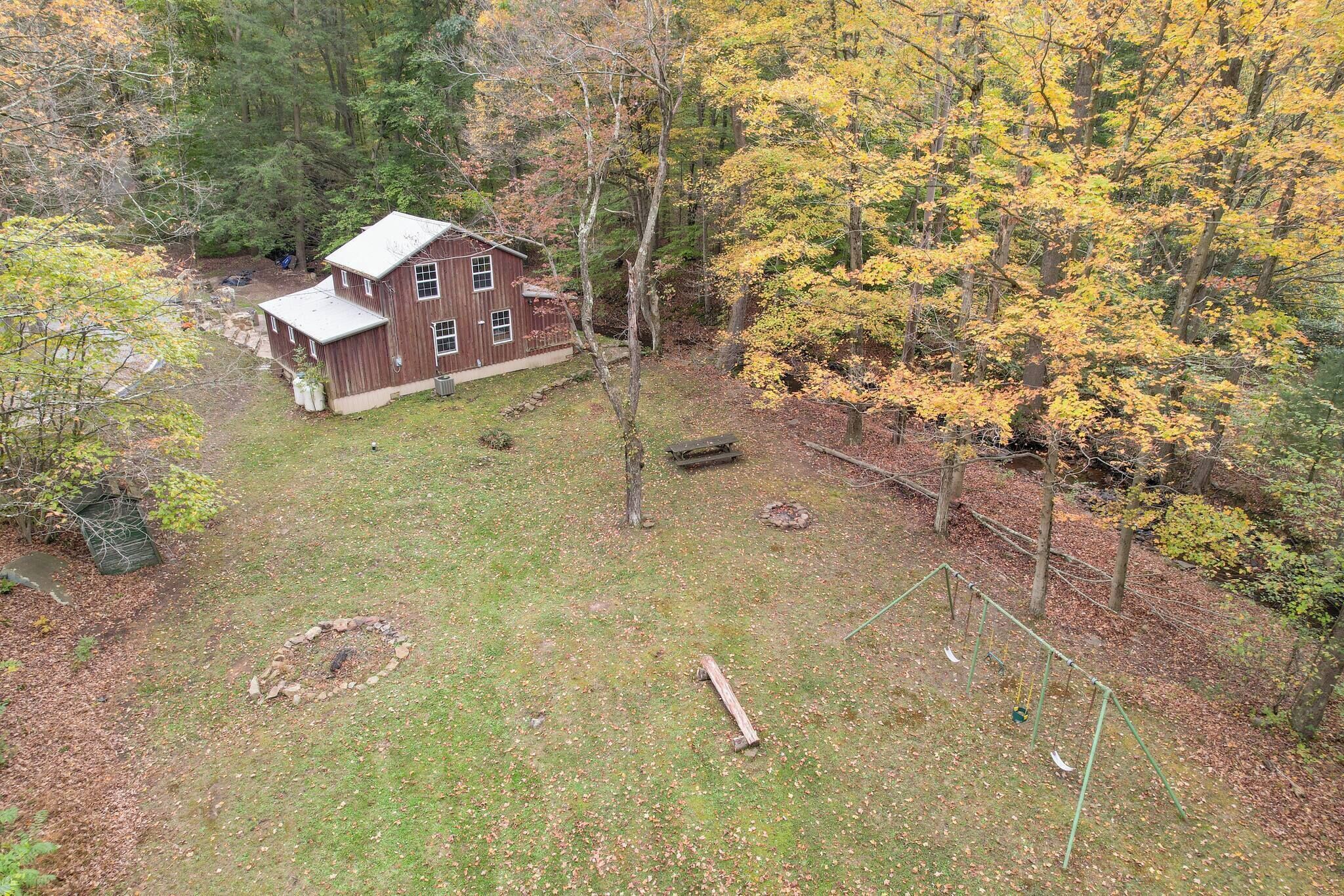 A rustic wooden house surrounded by a fenced yard with a swing set and a small pond.