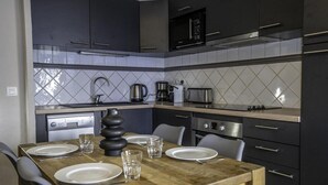 Une cuisine moderne avec des meubles de couleur sombre, une table à manger en bois mise avec des assiettes et des verres, une machine à café et un grille-pain.