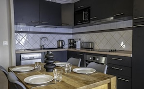 A modern kitchen with dark cabinets, a wooden dining table set with plates and glasses, a coffee maker, and a toaster.