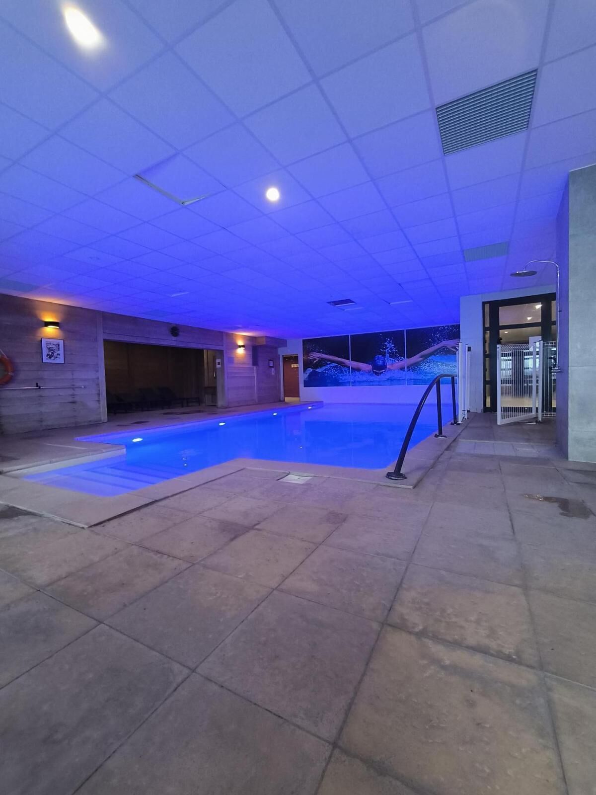 An indoor swimming pool with a tiled floor and a blue-lit ceiling.
