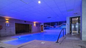 Une piscine intérieure avec un sol carrelé et un plafond éclairé en bleu.