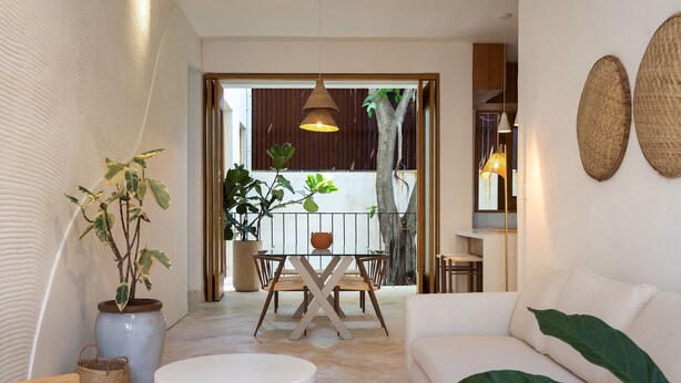 A modern living room with a white sofa, a round coffee table, and a dining area with a wooden table and chairs. There is a large potted plant and a hanging light fixture. - Boho Chic Oasis: 2BR + Family Room in Zona Colonial (SANTO DOMINGO)