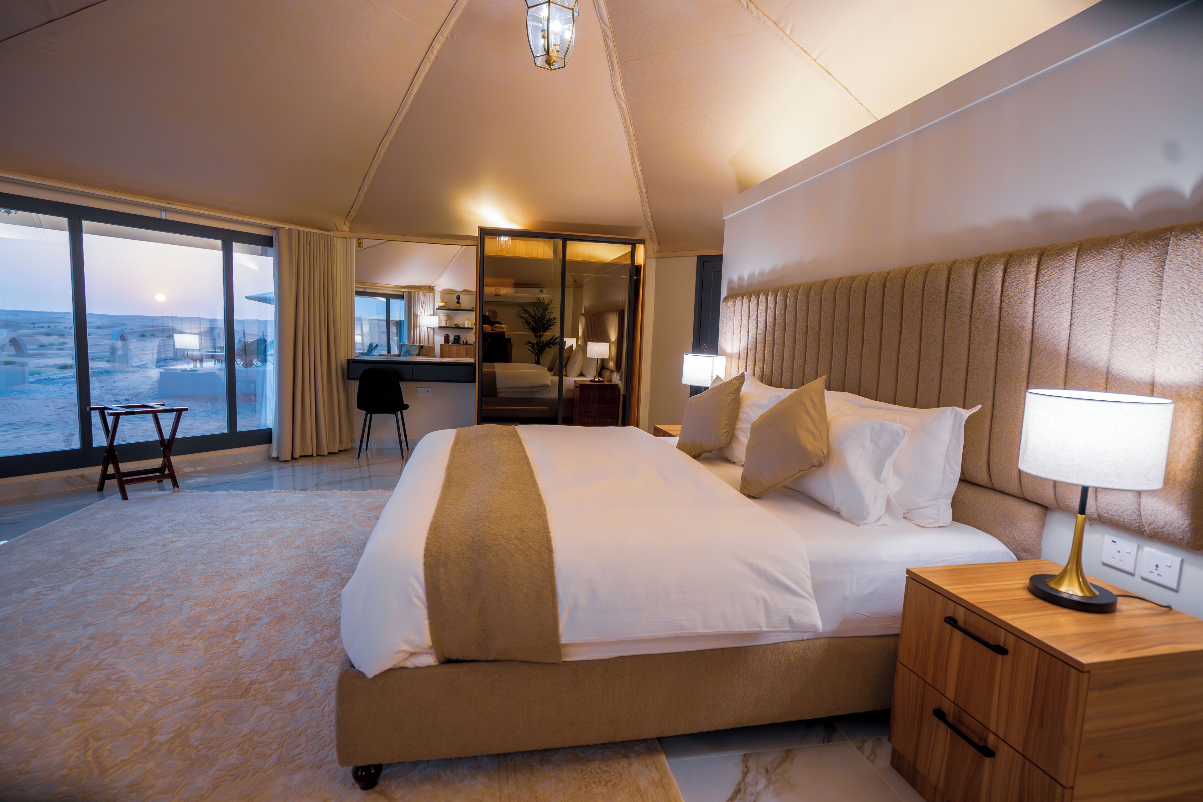 A spacious bedroom with a large bed, a nightstand, and a desk. There is a view of the ocean through large windows.