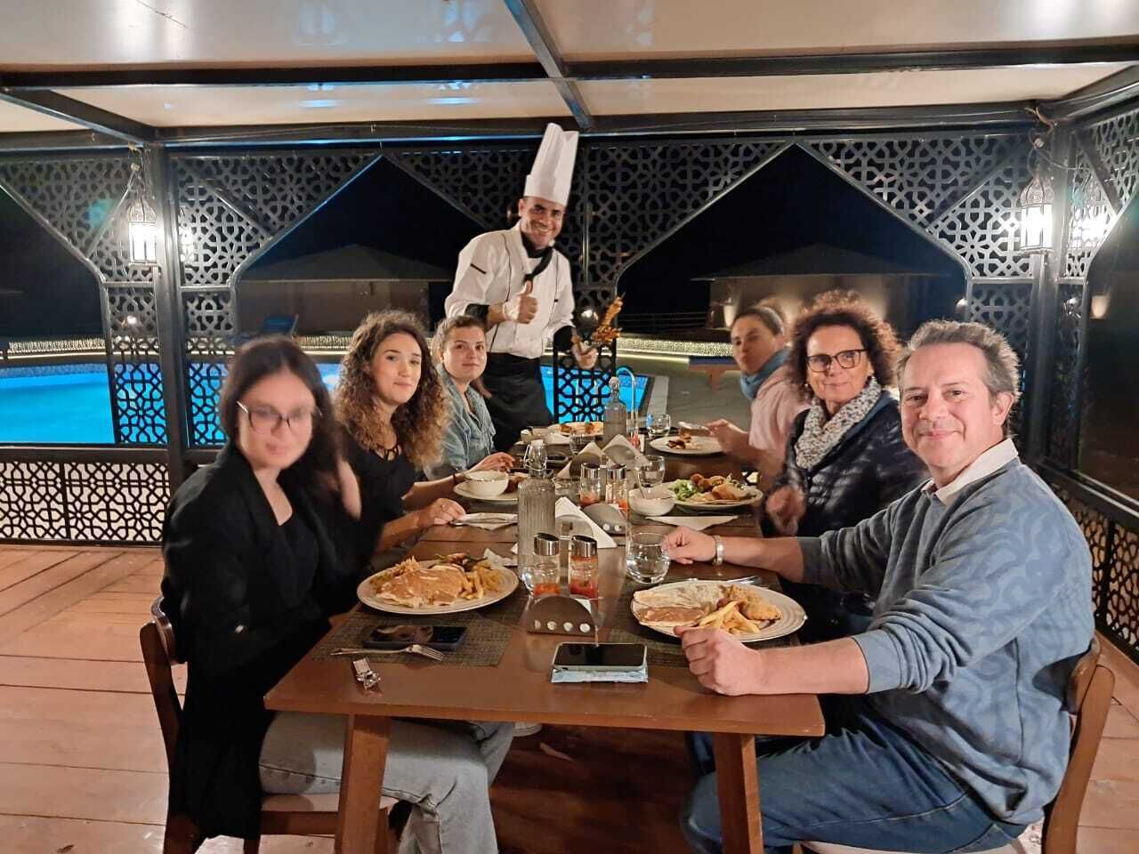 Un grupo de personas cenando en una mesa, con un chef detrás.
