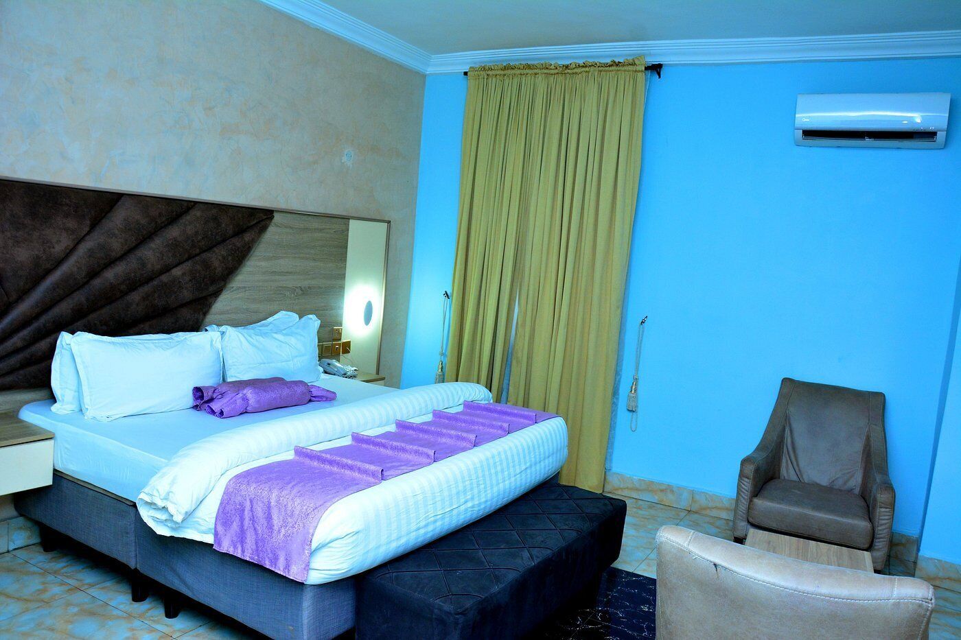 Una habitación de hotel con cama, silla, mesita de noche, espejo y aire acondicionado.