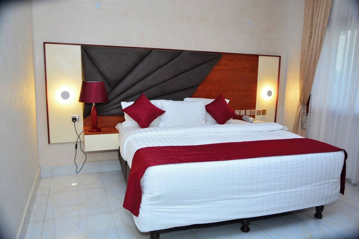 A neatly made bed with white linens and red accents, a modern headboard, and a bedside lamp.