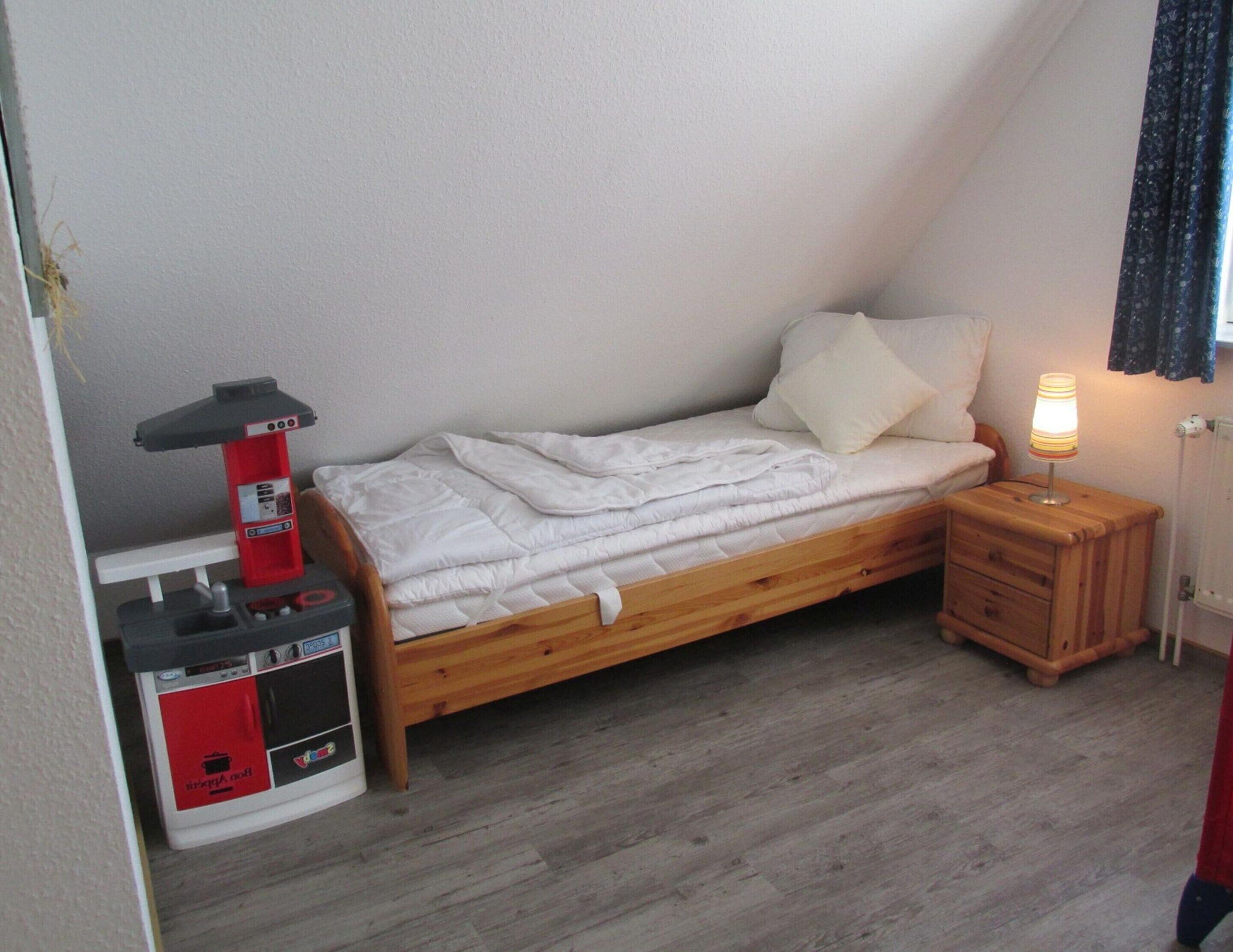 Una piccola camera con un letto singolo, una struttura letto in legno, un comodino con una lampada e un mobiletti rosso e bianco.