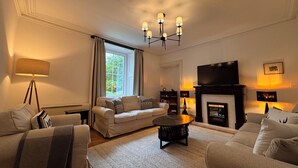 Una sala de estar con sofá, sillones, una mesa de centro, chimenea, televisión y una ventana con cortinas.