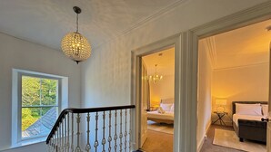 Una escalera con alfombra azul que conduce a un dormitorio con cama, mesita de noche y candelabro.