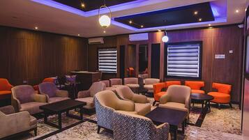 A modern lounge area with sofas, armchairs, and tables, featuring a marble floor and wooden paneling.