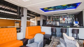 Zona de bar moderna con asientos naranja, una barra y un techo con un mural colorido.