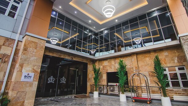 Un vestíbulo de hotel con diseño moderno, que cuenta con una amplia entrada de vidrio, un letrero de 'BON Hotels' y un mostrador de recepción.